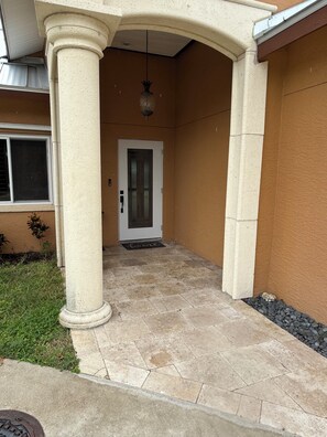 A covered outdoor area with a tiled floor, a door, and a hanging light fixture.