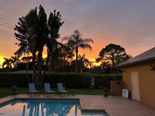 Ein Swimmingpool mit Liegestühlen, umgeben von Palmen und Blick auf den Sonnenuntergang.