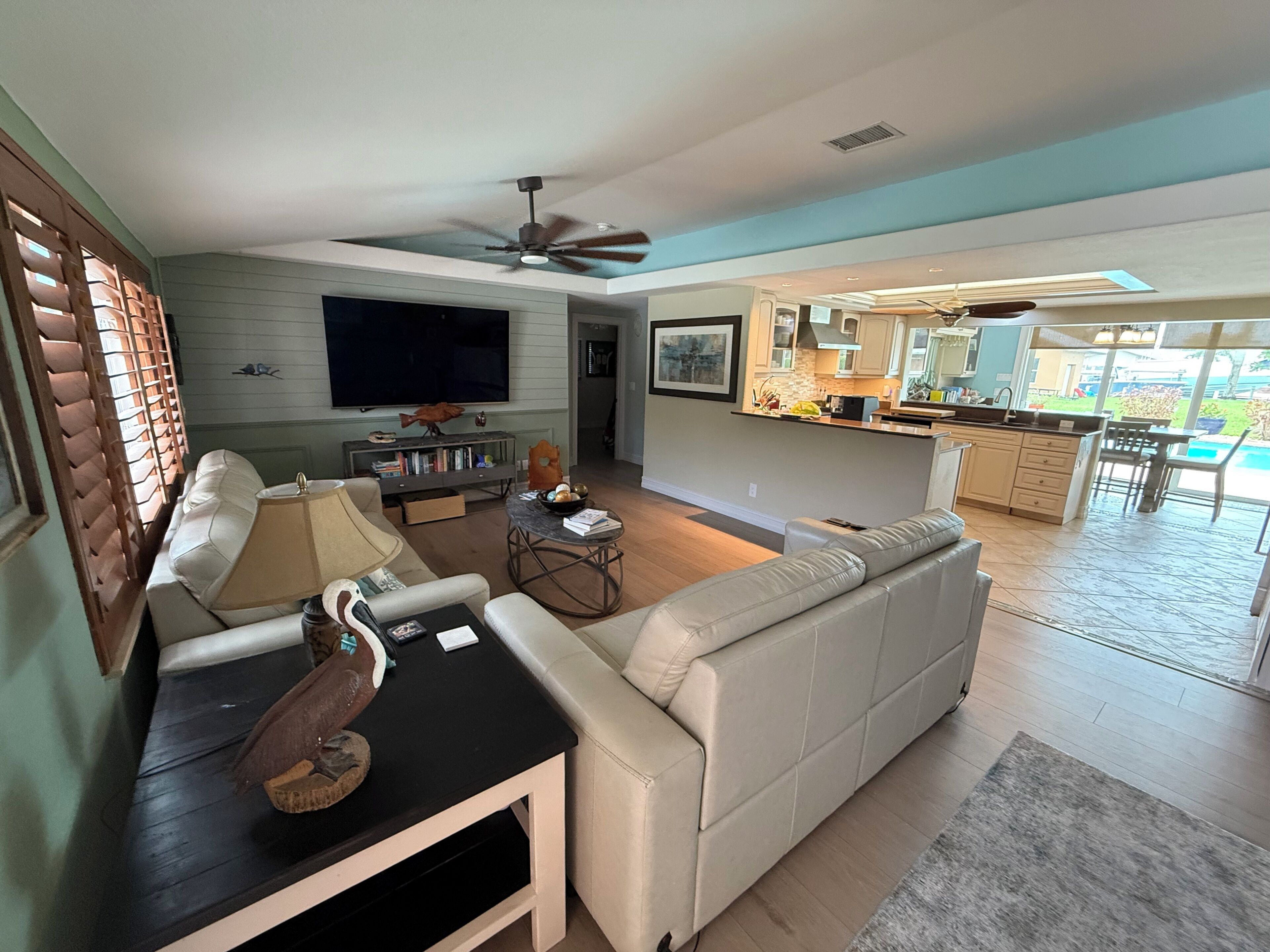 Una sala de estar moderna con un sofá, una mesa de centro y un televisor. Se ve una cocina con una barra y un comedor al fondo.