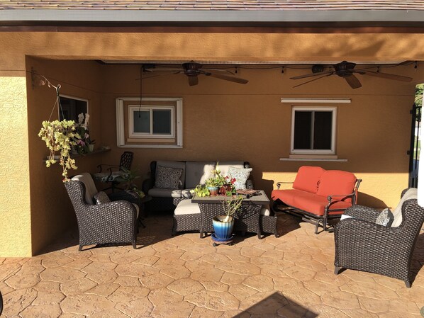 Eine Terrasse im Freien mit Korbmöbeln, einem roten Sofa und Topfpflanzen.