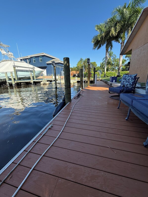 A wooden dock with a boat, a lounge chair, and a building in the background.