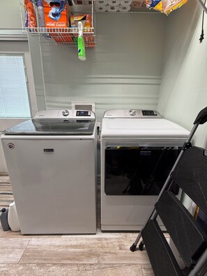 Deux machines à laver Maytag dans une pièce dont le sol est en bois et qui possède une fenêtre avec des stores.