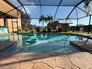 A swimming pool with a water toy, surrounded by a covered area with a view of houses and palm trees.