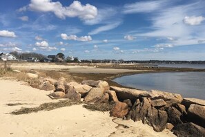 Un paysage côtier avec une plage de sable, de gros rochers et une étendue d’eau calme.
