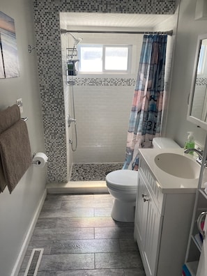 A bathroom with a shower, toilet, sink, and a towel rack.