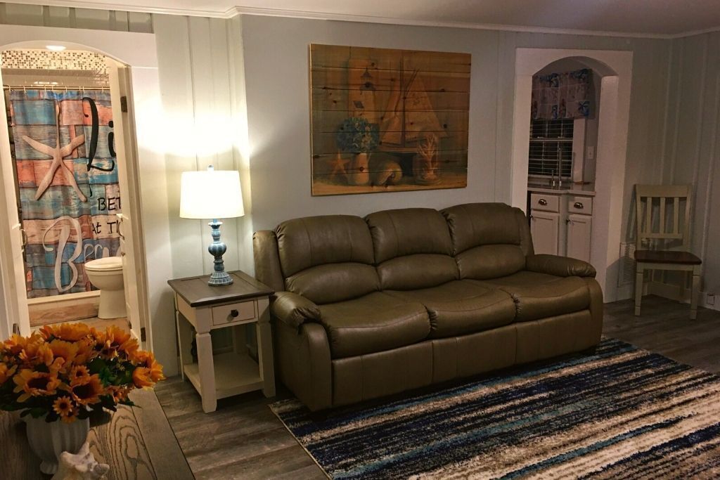 Un salon avec un canapé en cuir marron, un tapis à rayures, une lampe et un tableau accroché au mur.