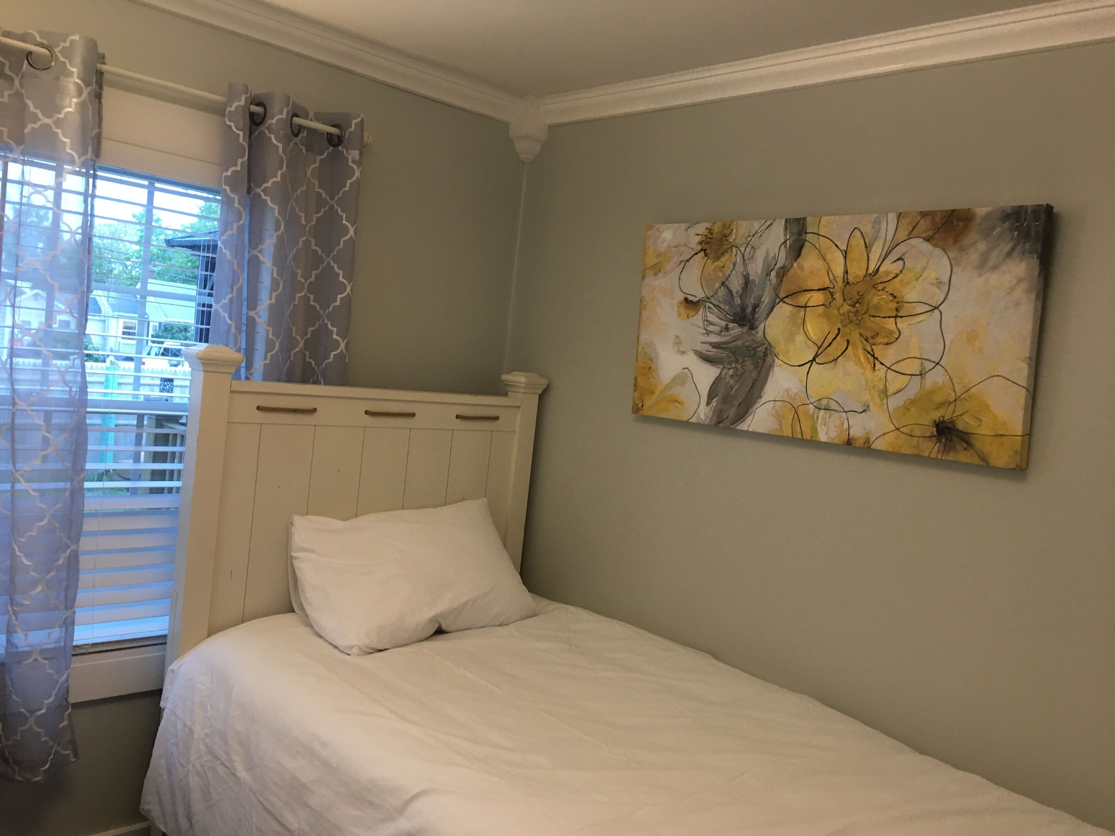 Un dormitorio con una cama individual, una ventana con persianas y un cuadro en la pared.