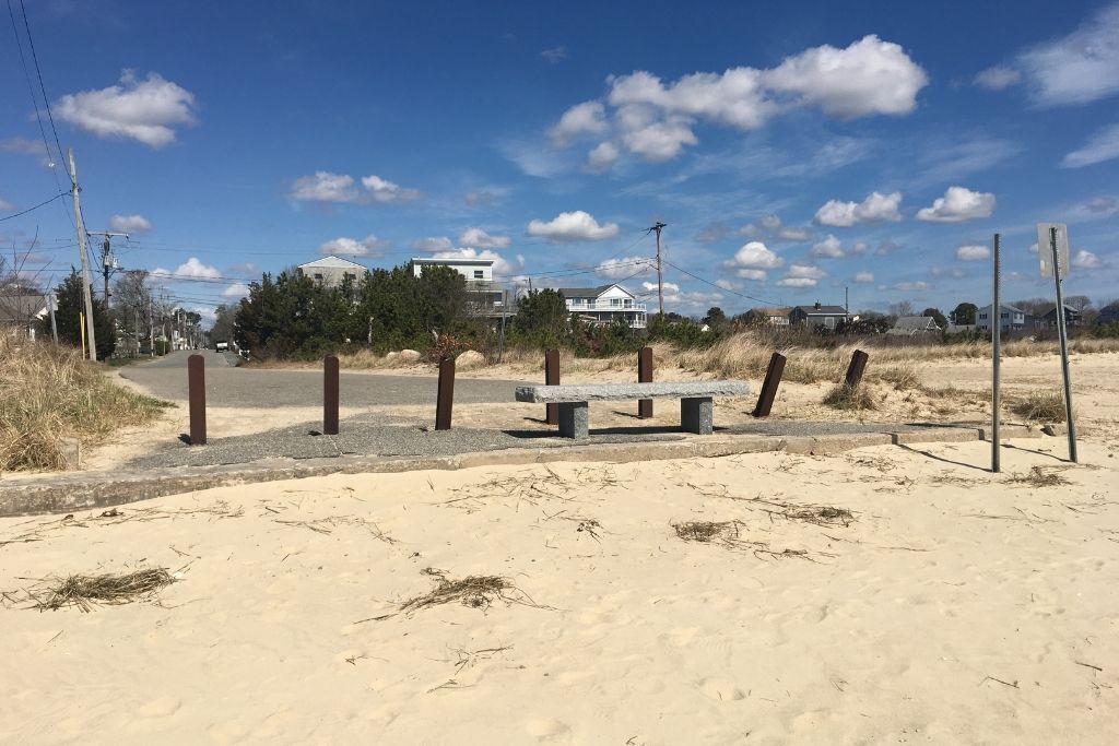 Una platja sorrenca amb una bosa i pals de fusta, cases al fons i un cel serè.
