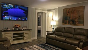Un salon avec un canapé en cuir, un téléviseur fixé au mur, une console sur laquelle est posé un vase de fleurs et un tableau accroché au mur.