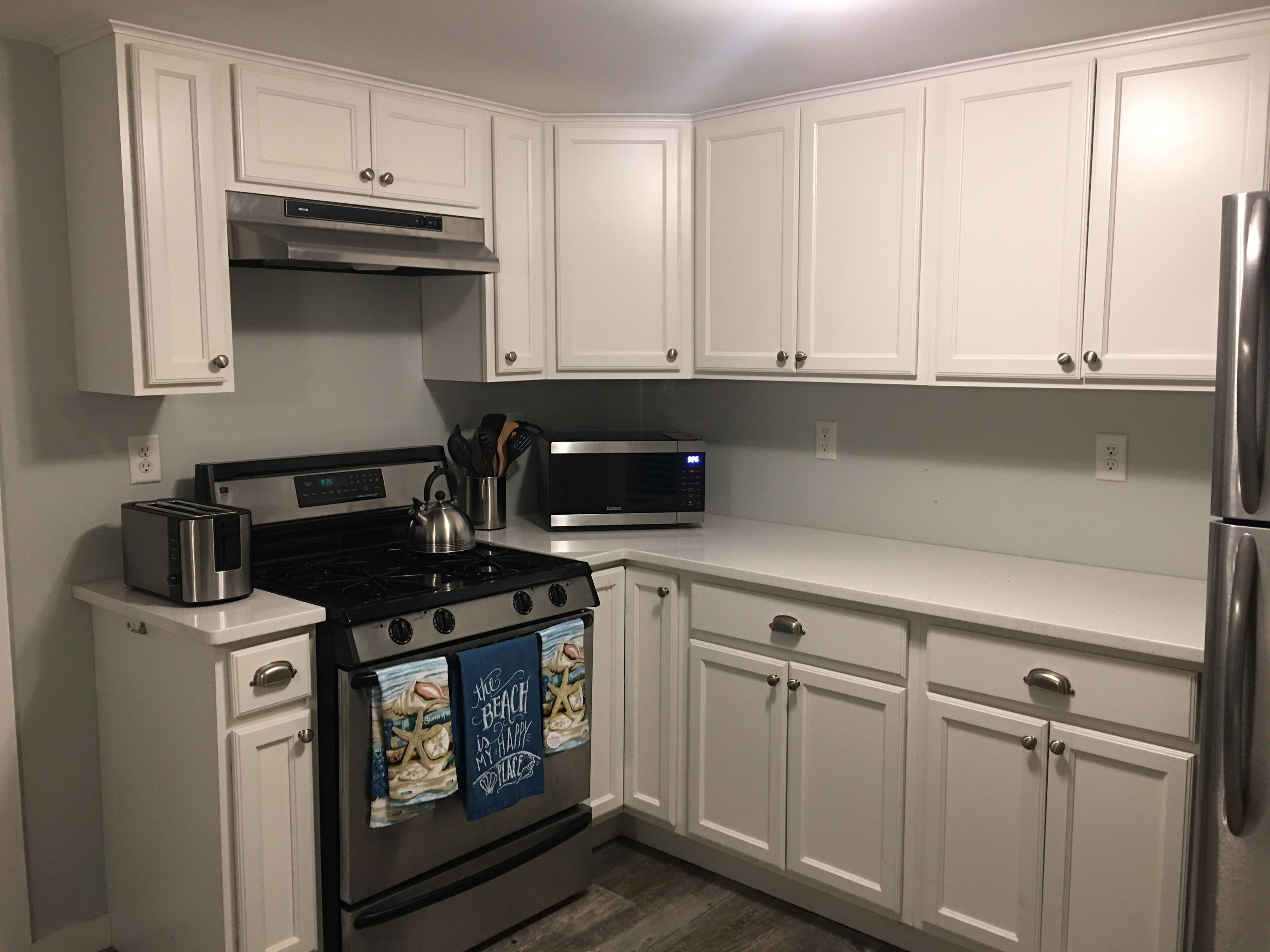 A kitchen with white cabinets, stainless steel appliances, and a microwave.