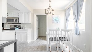 Een moderne keuken met witte kasten, een magnetron en een eethoek met een witte tafel en stoelen.
