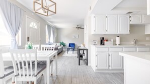 Een moderne keuken met witte kastjes, een eethoek met een witte tafel en stoelen, en een plafondventilator.