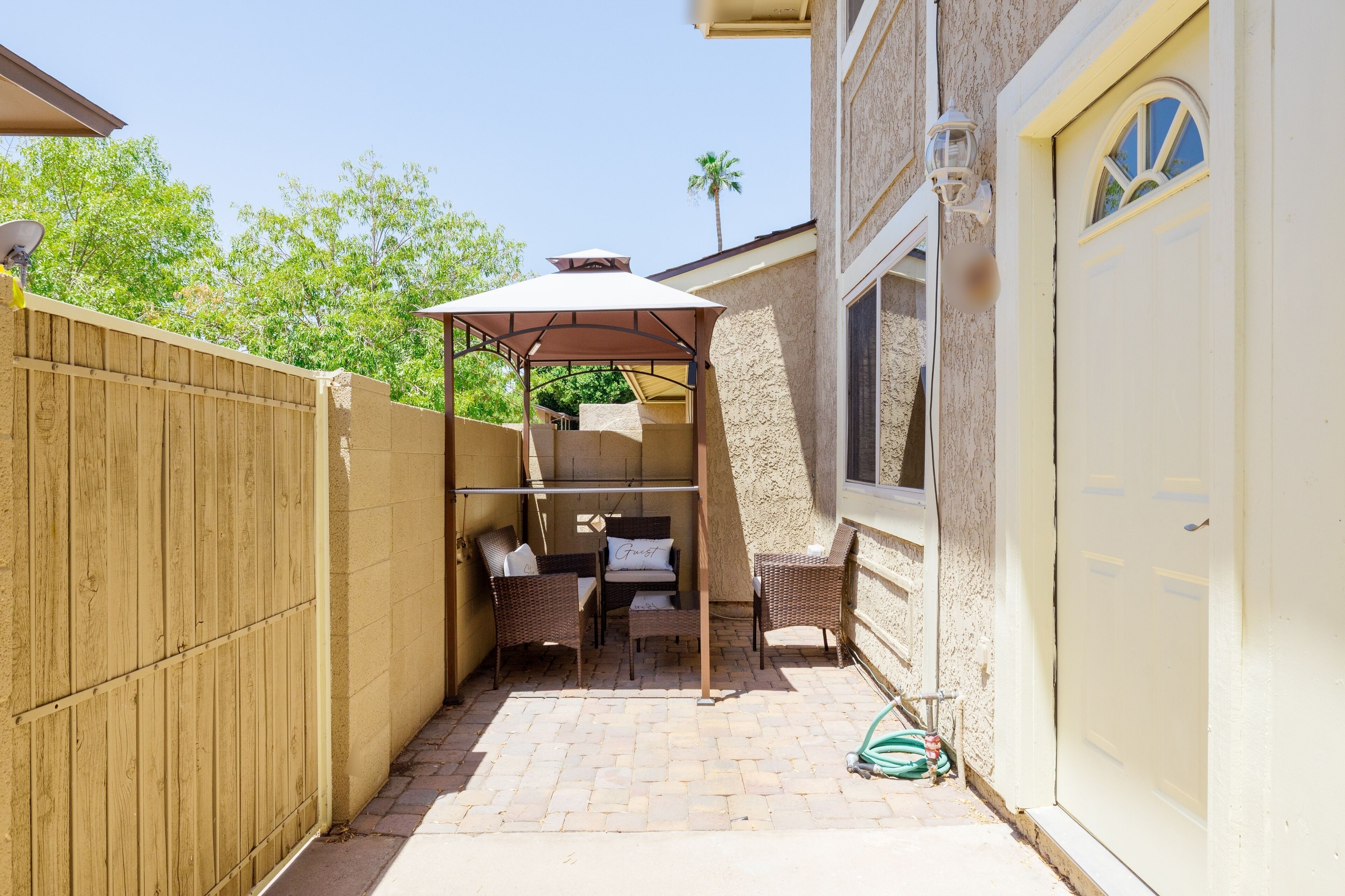 Un patio con zona de estar cubierta, cerca de madera y una casa con puerta de garaje.