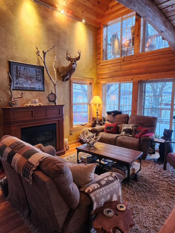 L’intérieur chaleureux d’un chalet en bois, avec une cheminée, des meubles confortables et une grande fenêtre donnant sur le paysage enneigé.