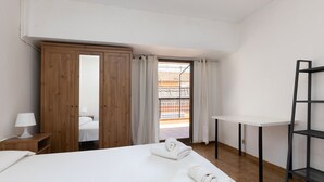 A bedroom with a bed, a wooden wardrobe, a desk, a chair, and a balcony view. - ATIC, PRIVATE TERRACE, 2 BEDROOMS (Barcelona)