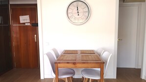 A dining area with a wooden table and white chairs, a wall clock, and a wooden door with a paper on it. - ATIC, PRIVATE TERRACE, 2 BEDROOMS (Barcelona)