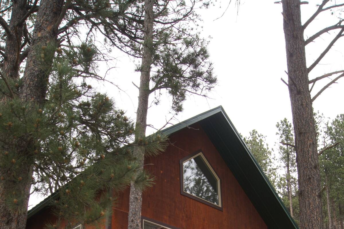 Una cabaña de madera con balcón, rodeada de árboles.