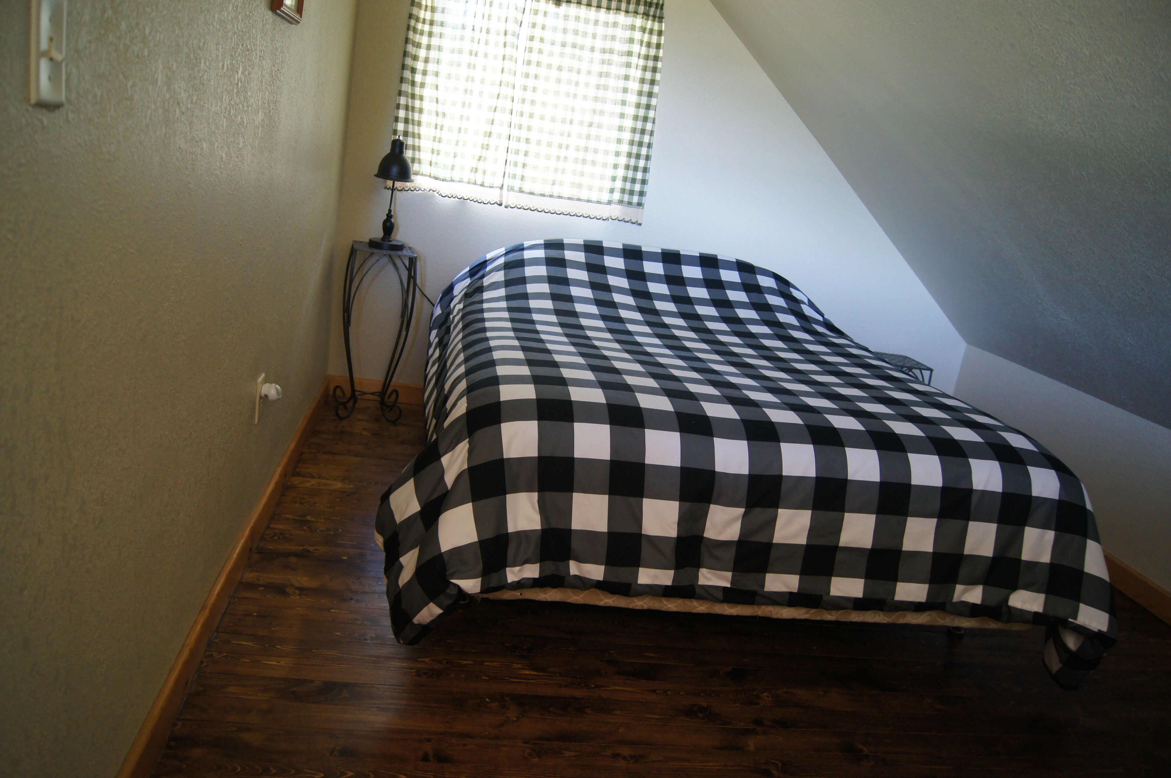 Une chambre à coucher avec une couvre-lit à carreaux, une lampe de chevet et une fenêtre ornée d’un rideau à carreaux.