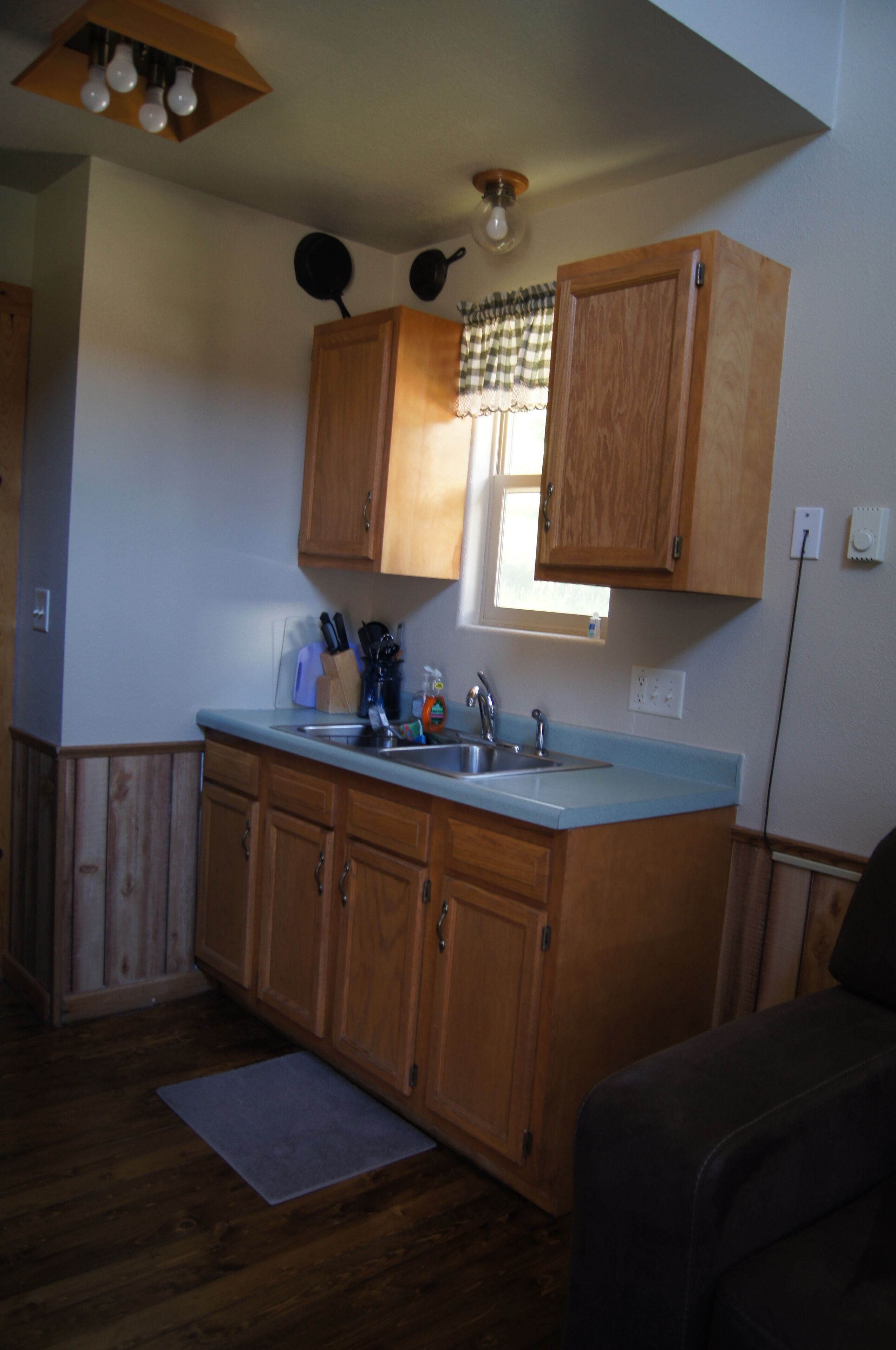 A kitchen with wooden cabinets, a countertop sink, and a window with a checkered valance.