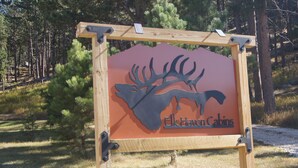Señal con silueta de ciervo y el texto "Elk Haven Cabins" en un entorno boscoso.