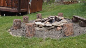Un hogar de piedra rodeado de troncos de árbol, con una terraza de madera y un edificio al fondo.