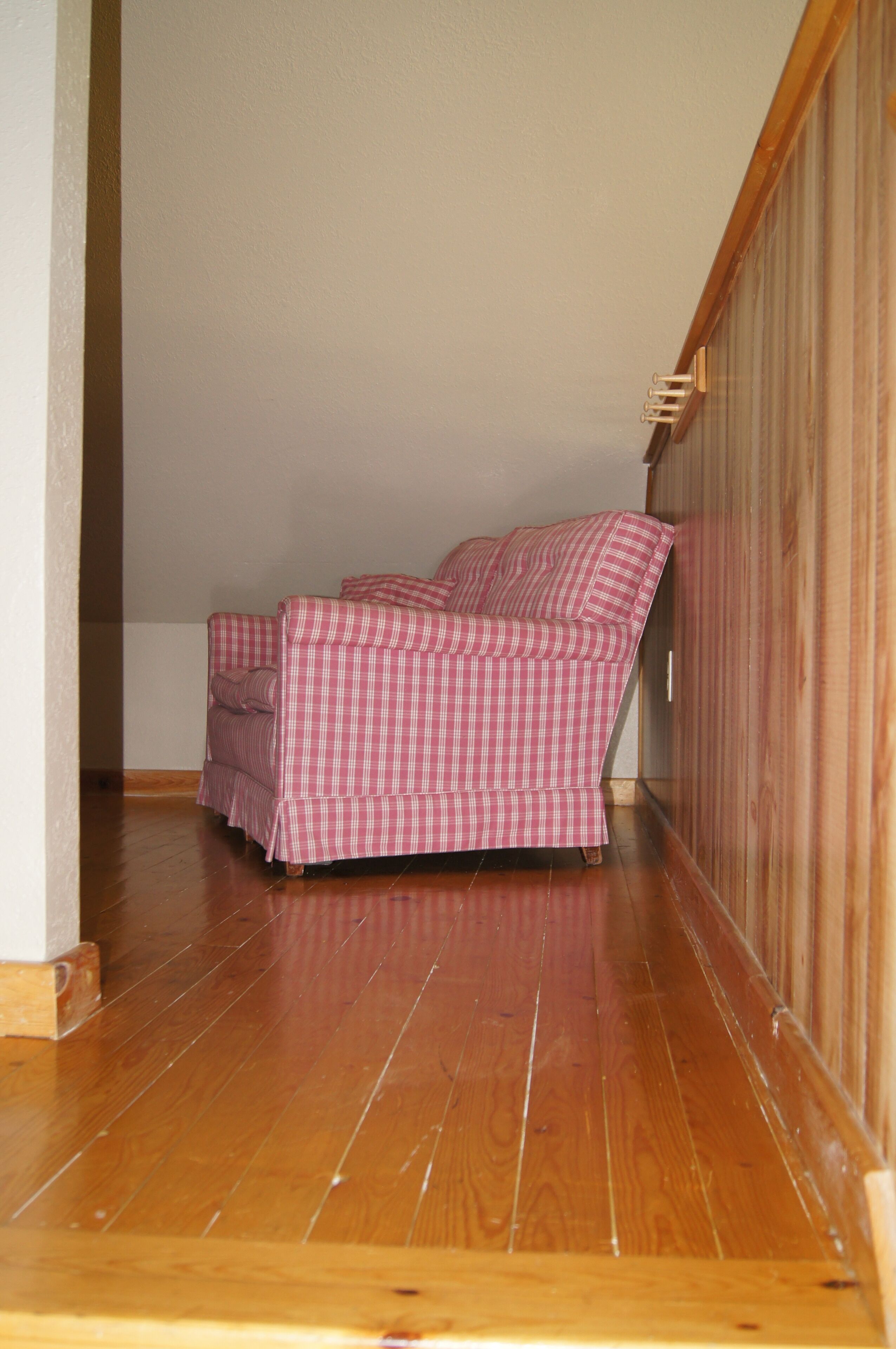 Una habitación de esquina con piso de madera, un sofá a cuadros y una pared de madera.