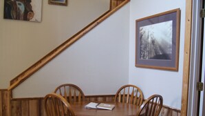 Un comedor con una mesa y sillas de madera, una escalera y obras de arte enmarcadas en las paredes.