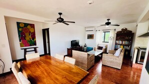 A spacious living area with a wooden dining table, wicker furniture, ceiling fans, a bookshelf, and a television. - Stunning Rooftop Villa with Breathtaking Caribbean Views & Large Private Terrace (San Miguel de Cozumel)