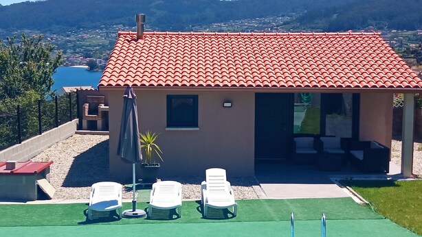 A building with a red-tiled roof, a pool with a ladder, and white lounge chairs. - COZY GUEST HOUSE (BUEU)