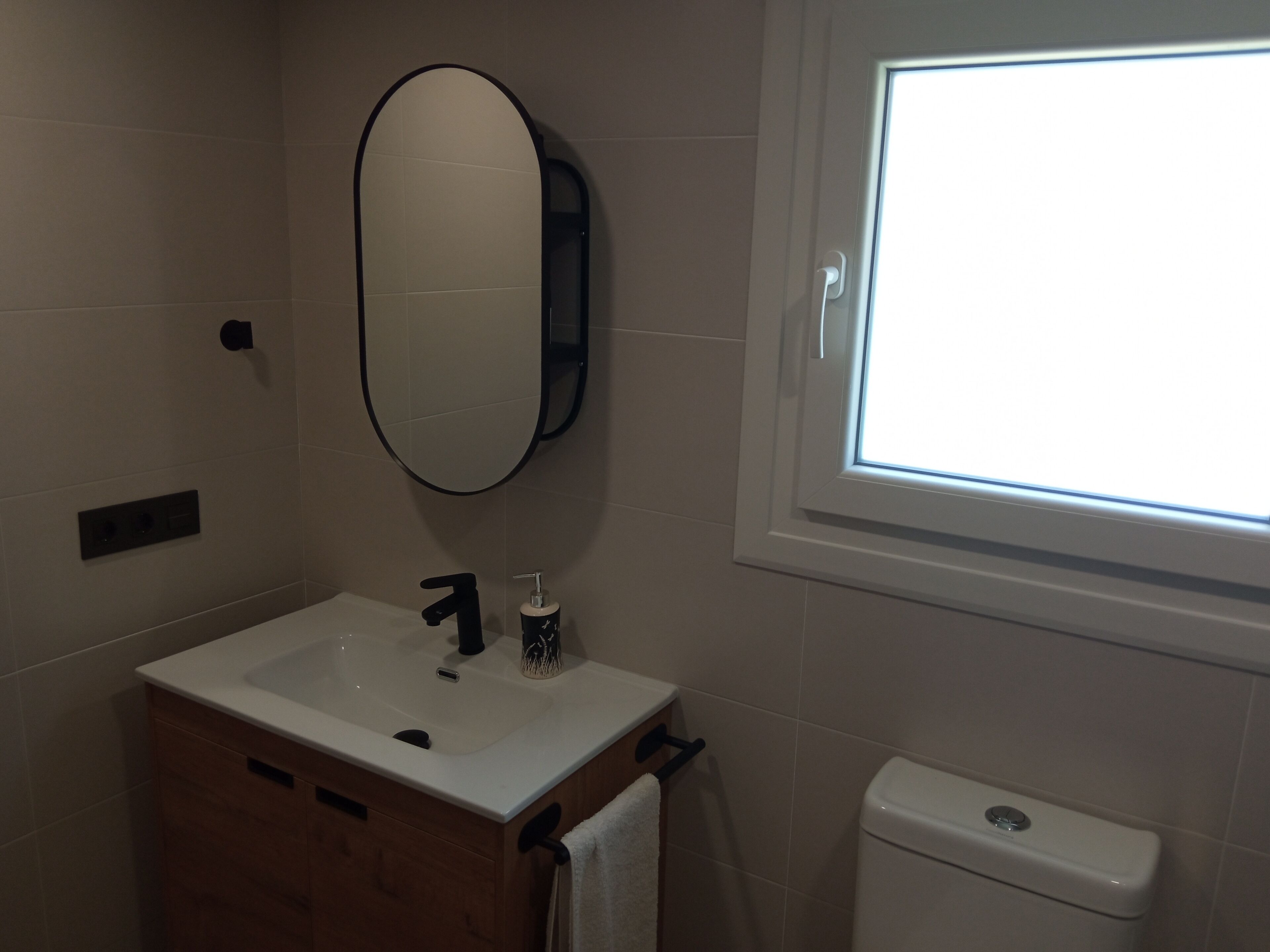 A bathroom with a white sink, black faucet, and a mirror above it. There is a window with a view of the sky.