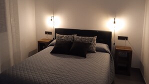A neatly made bed with a quilted cover, two bedside tables with lamps, and a plain white wall. - COZY GUEST HOUSE (BUEU)