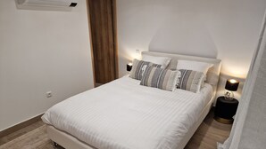 Un lit bien fait, avec du linge de lit blanc et des oreillers à rayures, une table de chevet avec une lampe, et une porte en bois en arrière-plan.