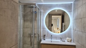 Une salle de bain moderne avec une douche à parois de verre, un miroir rond et un meuble-lavabo en bois.
