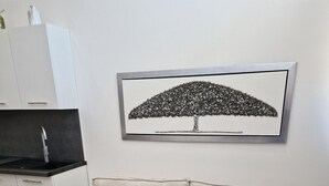 Un salon moderne avec un canapé beige, une table basse noire et une œuvre d’art représentant un arbre en noir et blanc, encadrée et accrochée au mur.