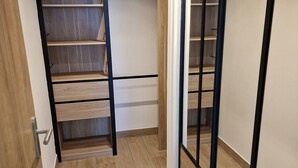 Un couloir étroit avec un plancher en bois, une porte coulissante sur la droite et un escalier avec une rampe en métal noir sur la gauche.