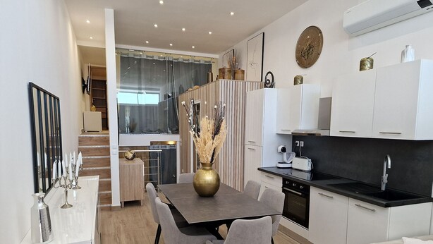 Une cuisine moderne avec un coin repas, comprenant un plan de travail noir, des meubles blancs et une table à manger avec des chaises.