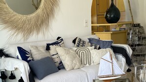 Een woonkamer met een bank, een rond voetenbankje, gevlochten manden en een grote spiegel.