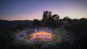 Una casa con terraza y luces colgantes, rodeada de árboles y colinas.