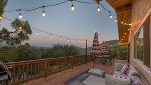 Una terraza de madera con luces colgantes, mobiliario exterior y vistas al paisaje.