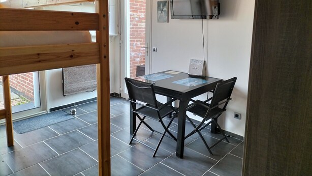 A dining area with a table and chairs, a TV mounted on the wall, and a wooden partition. - Studio near the beach (Criel-sur-Mer)
