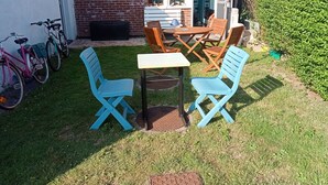 A patio area with a table and two blue chairs, a brick wall, and a window. - Studio near the beach (Criel-sur-Mer)
