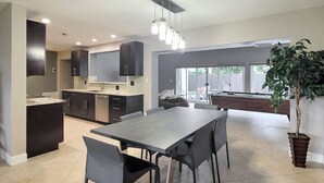 A modern kitchen with dark cabinets, a dining area with a pool table, and a potted plant.