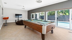 A pool table in a room with a large window, a television, and a bean bag chair.