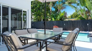 An outdoor patio with a glass table and chairs, a pool, and a view of tropical vegetation.