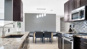 A modern kitchen with dark cabinets, a large island with a sink, a built-in oven, and a microwave.