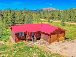 A wooden cabin with a red roof, a garage, and a staircase leading to the entrance. - 25 mi Breck | Stargazing | Hot Tub | King Beds (Fairplay)