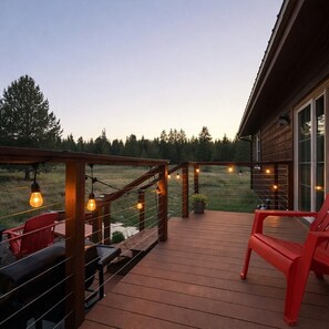 A wooden deck with outdoor seating, string lights, and a view of a grassy field. - 25mi to Breck | Hot Tub&Fire Pit | Stocked Kitchen (Fairplay)