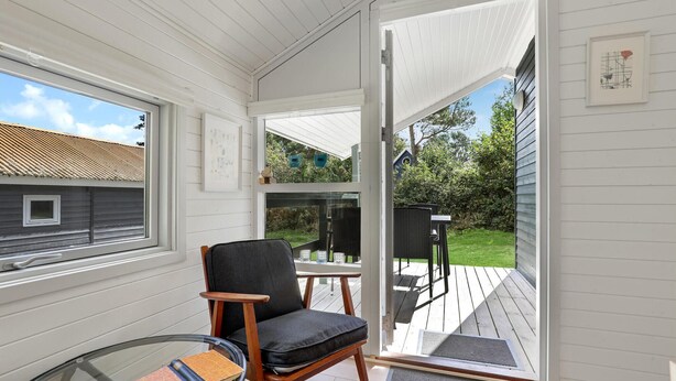 Ein gemütliches Zimmer mit Schiebetür zum Balkon, ein bequemer Sessel, ein kleiner Tisch und ein Glastisch mit Büchern.