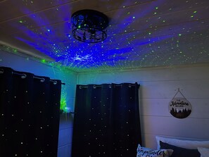 Een kamer met een sterrenhemelplafond, een bord aan de muur en een bed met een kussen.