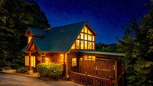A wooden cabin with a sloped roof, large windows, and a fenced porch under a starry night sky. - Hot tub cabin near Pigeon Forge, game room, mountain views (Sevierville)